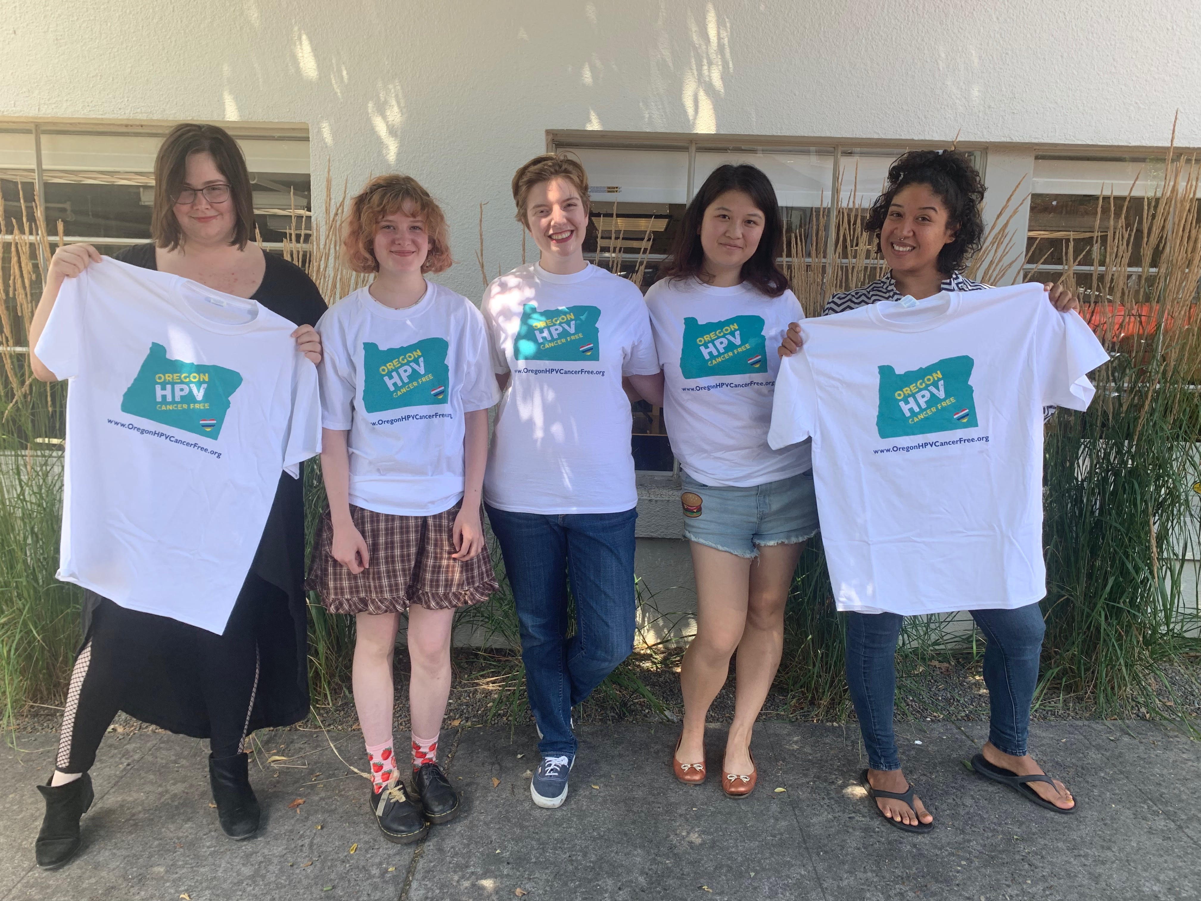 Four students and one OSBHA employee standing in front of white building wearing & holding up HPV week t-shirts